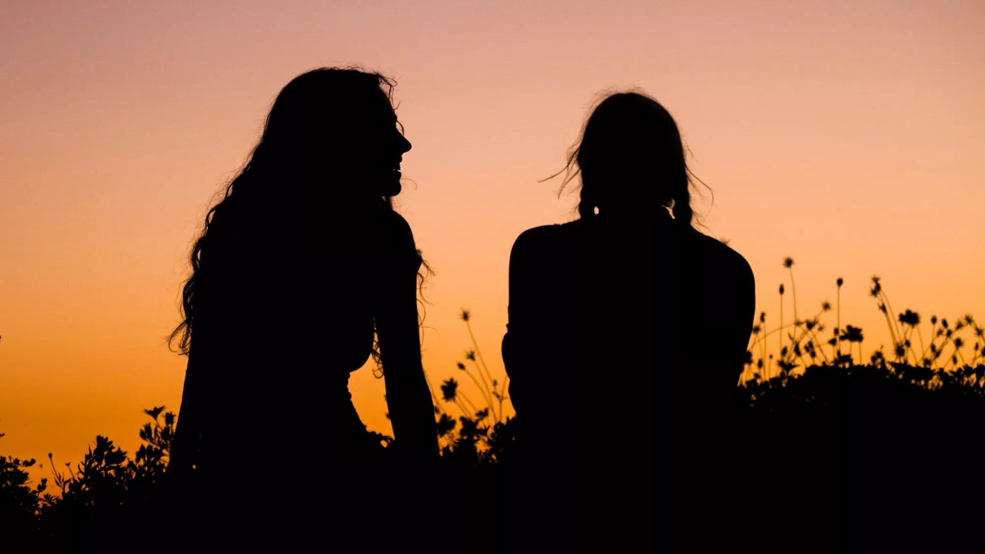 两个长发的人在聊天，夕阳映衬出他们的剪影