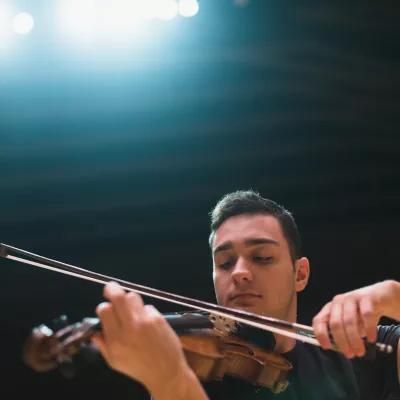 一个学生在灯光下的舞台上拉小提琴.