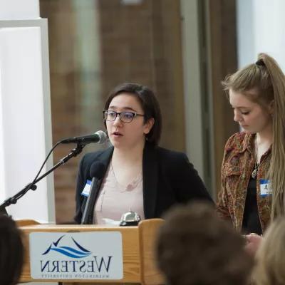 两名学生站在带有西方标志的讲台上发言.