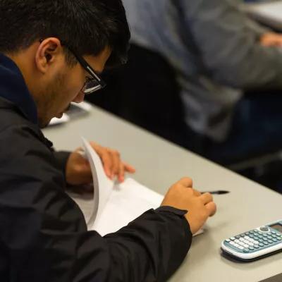 一个学生坐在桌子旁看试卷，旁边放着一个计算器.
