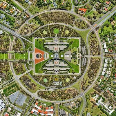 堪培拉议会大厦鸟瞰图，澳大利亚. 一个大型的绿色长方形校园，围绕着议会大楼，四周环绕着巨大的回旋镖墙. 都被同心圆的道路包围着. 议会大厦显然是这座城市其余部分的中心.